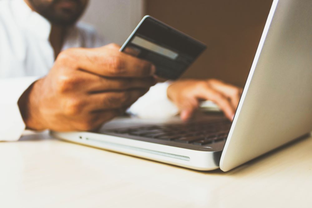 Close up of a person holding a credit card with one hand and typing on a laptop with the other.