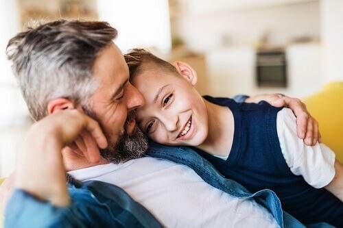 Smiling father sitting with his arm around his smiling son.